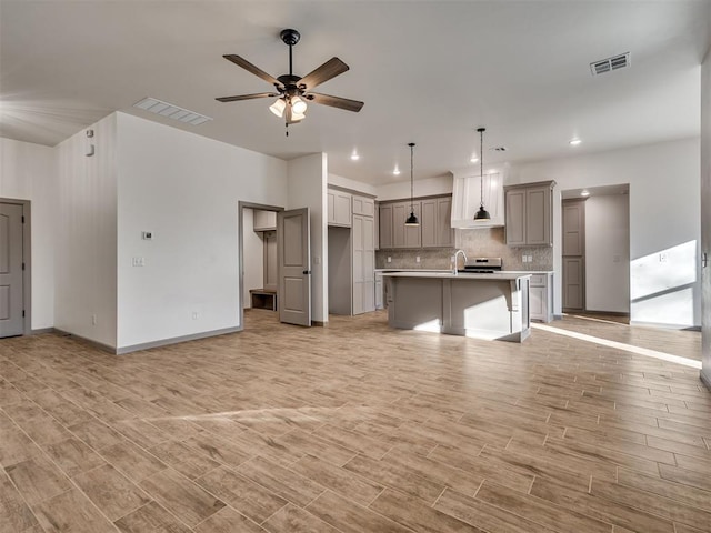 kitchen with ceiling fan, gray cabinetry, hanging light fixtures, backsplash, and a center island with sink