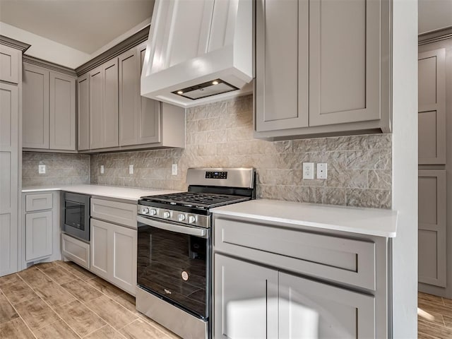 kitchen with gray cabinets, stainless steel range with gas cooktop, ventilation hood, built in microwave, and backsplash