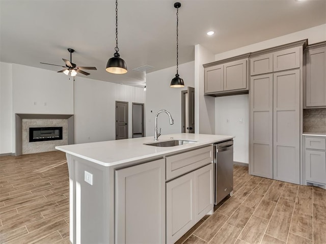 kitchen with hanging light fixtures, gray cabinets, dishwasher, and a center island with sink