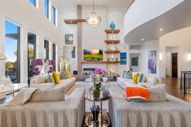 living room with a towering ceiling, dark hardwood / wood-style flooring, an inviting chandelier, and a brick fireplace