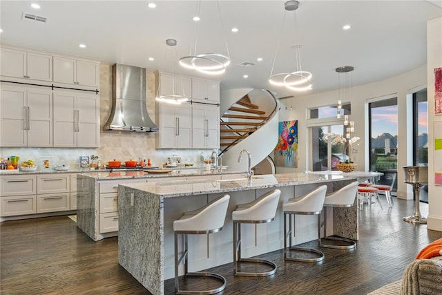 kitchen with a large island, dark hardwood / wood-style flooring, wall chimney range hood, and hanging light fixtures