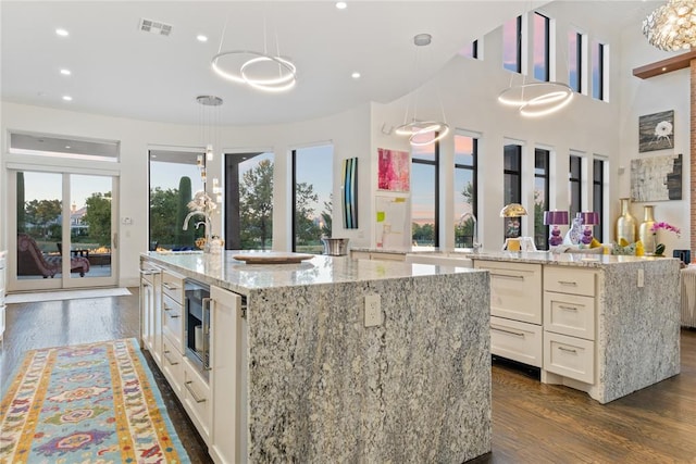 kitchen with dark wood-type flooring, sink, decorative light fixtures, light stone countertops, and a large island