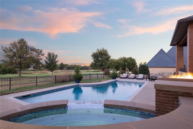 pool at dusk featuring an in ground hot tub and an outdoor fire pit