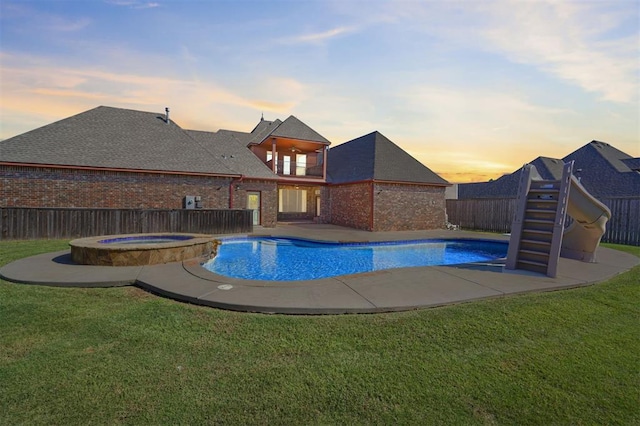 pool at dusk with a lawn and an in ground hot tub