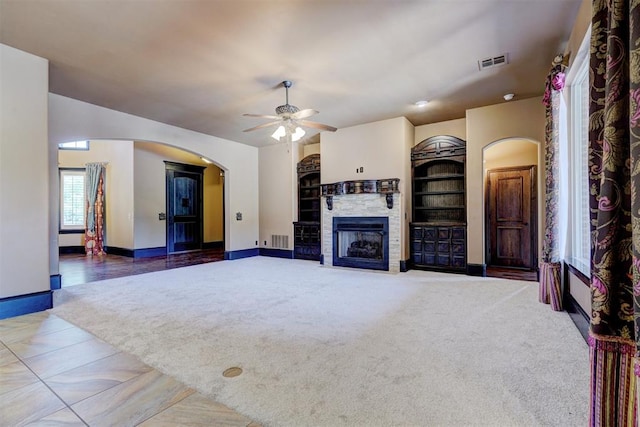 unfurnished living room featuring carpet flooring, built in shelves, ceiling fan, and a fireplace