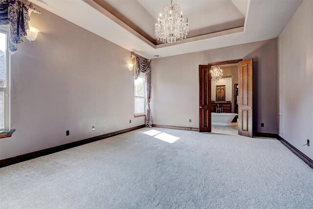 unfurnished bedroom featuring a tray ceiling, ensuite bath, carpet flooring, and an inviting chandelier