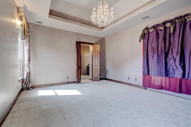 carpeted empty room with a chandelier and a raised ceiling