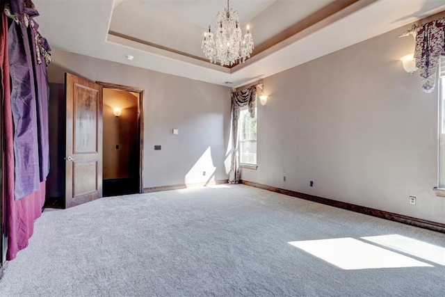 unfurnished room with a chandelier, carpet floors, and a raised ceiling