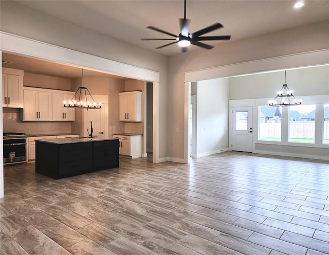 kitchen with stainless steel oven, light hardwood / wood-style flooring, a center island with sink, white cabinets, and ceiling fan with notable chandelier