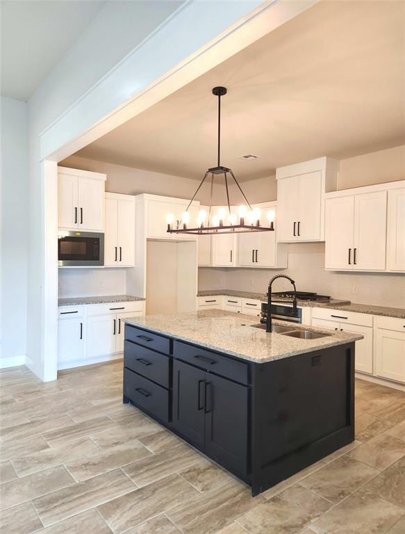 kitchen with pendant lighting, a center island with sink, white cabinetry, and a notable chandelier