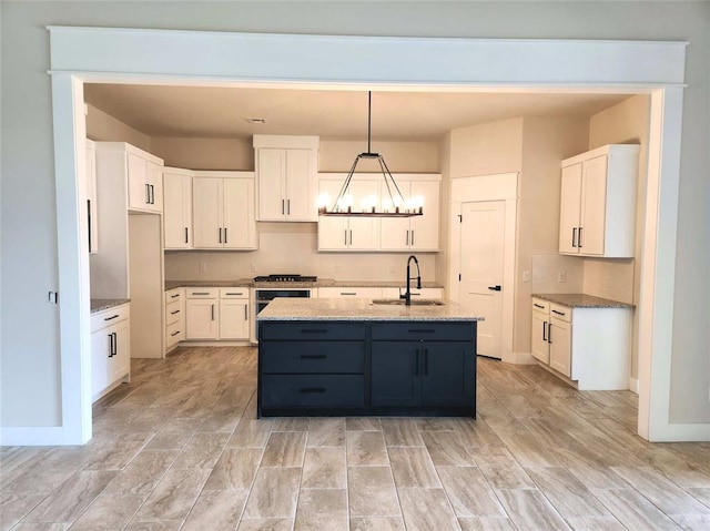 kitchen with white cabinets, a center island with sink, hanging light fixtures, light hardwood / wood-style floors, and light stone counters