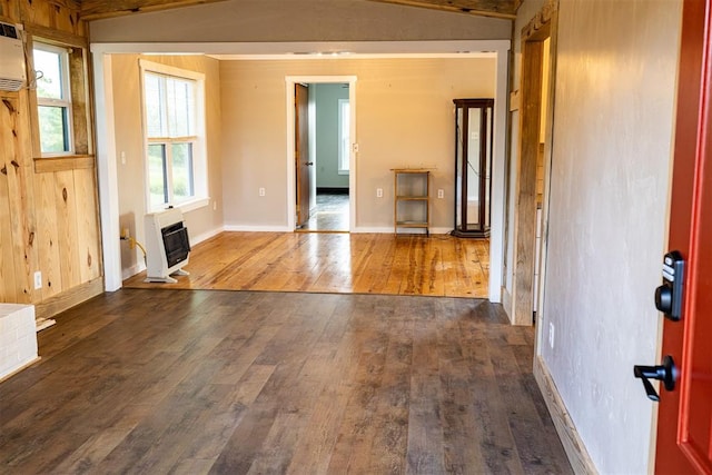 empty room with a wood stove, dark hardwood / wood-style floors, a wall unit AC, heating unit, and vaulted ceiling