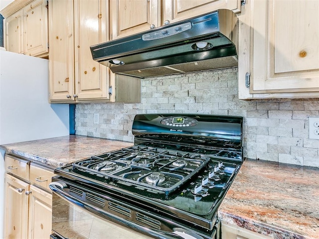 kitchen featuring black gas range, backsplash, light stone countertops, and light brown cabinets