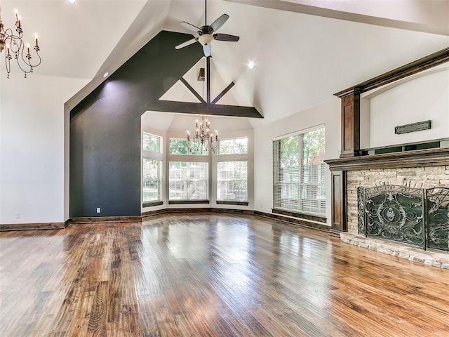 unfurnished living room with ceiling fan with notable chandelier, a stone fireplace, wood-type flooring, and high vaulted ceiling