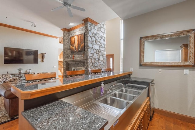 kitchen featuring kitchen peninsula, ceiling fan, a stone fireplace, and light wood-type flooring