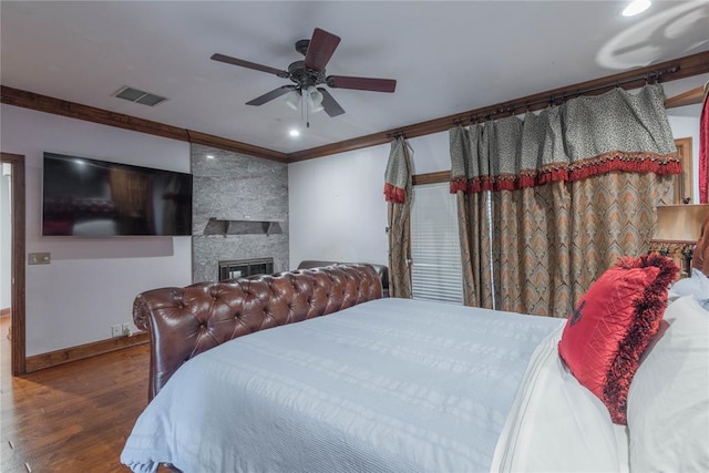 bedroom with hardwood / wood-style flooring, ceiling fan, a large fireplace, and ornamental molding