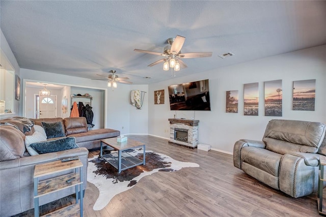 living room featuring a stone fireplace, wood-type flooring, and ceiling fan