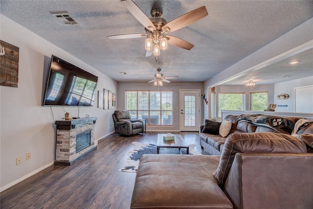 living room with ceiling fan, a stone fireplace, dark wood-type flooring, and a textured ceiling