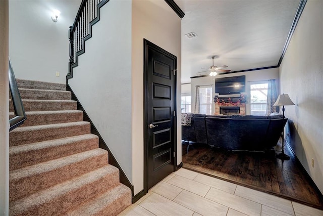 stairway featuring wood-type flooring, a stone fireplace, ceiling fan, and ornamental molding