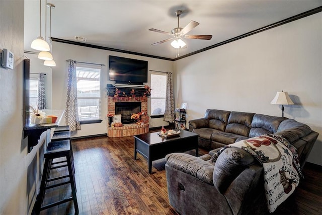 living room featuring dark hardwood / wood-style floors, ceiling fan, crown molding, and a brick fireplace