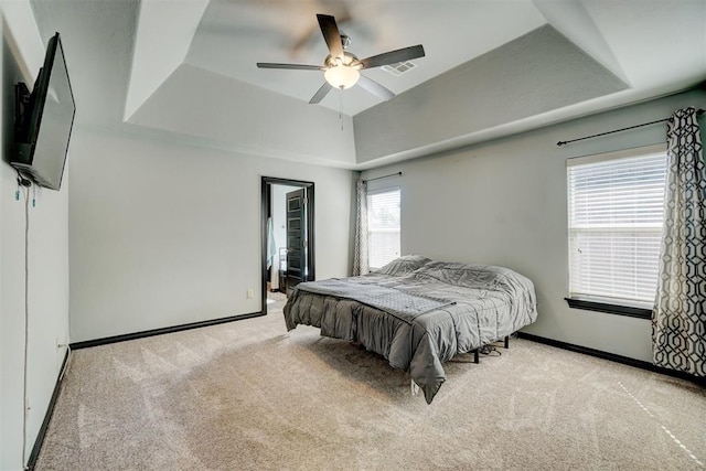 carpeted bedroom with ceiling fan, a raised ceiling, and multiple windows