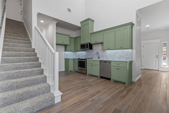 kitchen with light hardwood / wood-style flooring, ornamental molding, green cabinetry, and appliances with stainless steel finishes