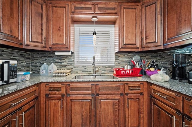 kitchen featuring pendant lighting, decorative backsplash, sink, and stone counters