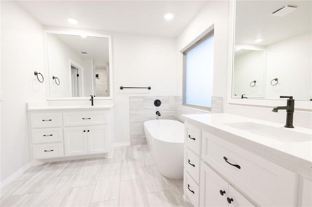 full bath with visible vents, a sink, a freestanding bath, two vanities, and recessed lighting