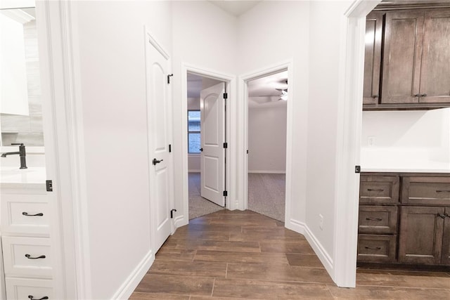 hall featuring dark wood-style flooring, a sink, and baseboards