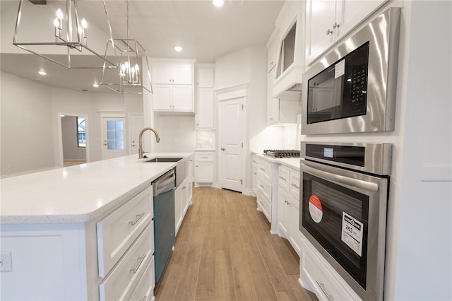 kitchen with a sink, white cabinetry, stainless steel appliances, light wood-style floors, and hanging light fixtures