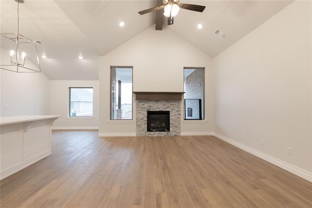 unfurnished living room featuring baseboards, visible vents, a fireplace, ceiling fan with notable chandelier, and light wood-type flooring