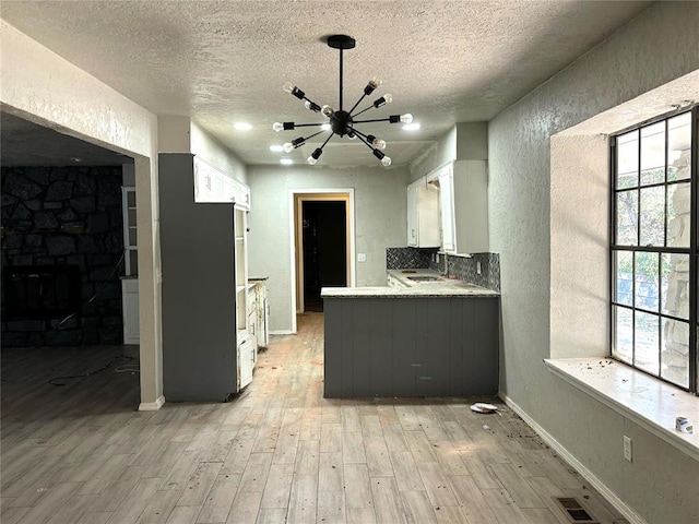 kitchen featuring light wood-type flooring, a textured ceiling, sink, a notable chandelier, and white cabinetry