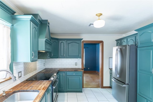 kitchen featuring butcher block counters, sink, stainless steel appliances, wall chimney range hood, and crown molding