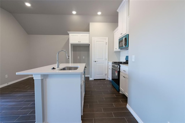 kitchen featuring range with gas cooktop, stainless steel microwave, white cabinetry, a sink, and an island with sink