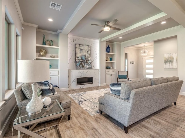 living room featuring built in shelves, wood-type flooring, ceiling fan with notable chandelier, and ornamental molding