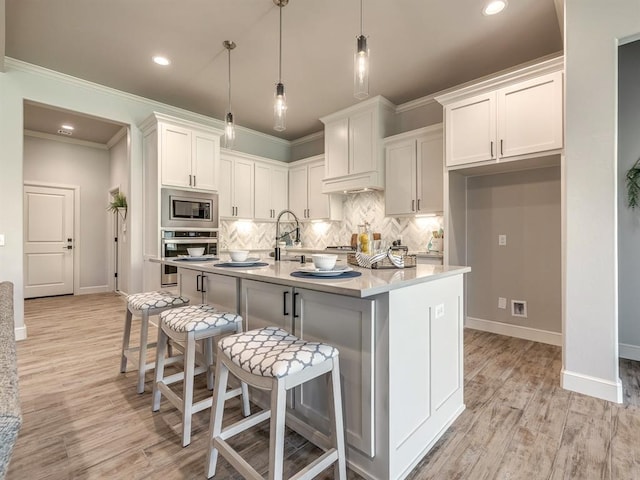 kitchen with appliances with stainless steel finishes, a kitchen island with sink, decorative light fixtures, light hardwood / wood-style flooring, and white cabinets