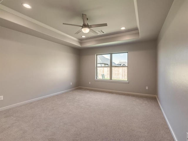 empty room with a tray ceiling, crown molding, and light colored carpet