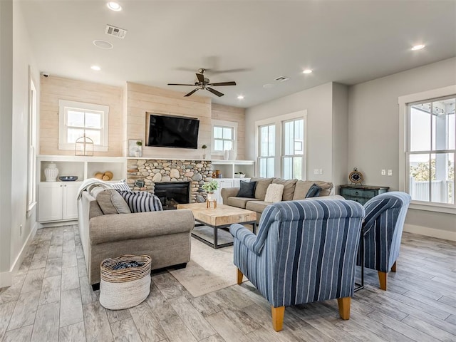 living room with light hardwood / wood-style flooring, ceiling fan, and a stone fireplace