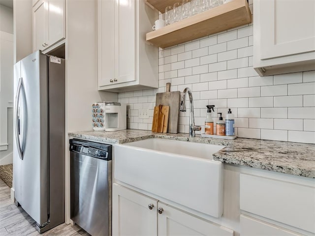 kitchen featuring white cabinets, light stone countertops, appliances with stainless steel finishes, and light hardwood / wood-style flooring