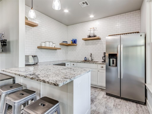 kitchen with stainless steel fridge, a kitchen breakfast bar, sink, light hardwood / wood-style flooring, and white cabinetry