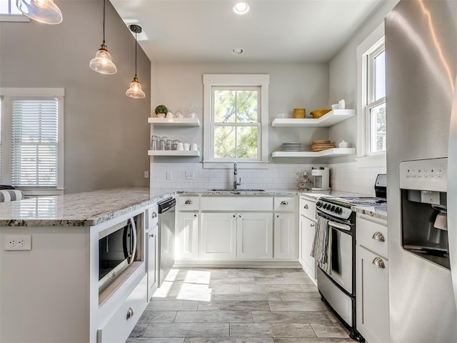 kitchen with sink, kitchen peninsula, decorative light fixtures, white cabinets, and appliances with stainless steel finishes