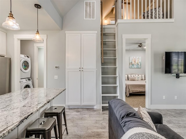 kitchen with white cabinetry, light stone countertops, hanging light fixtures, stacked washer and dryer, and lofted ceiling