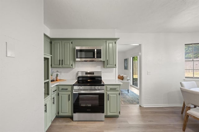 kitchen with stainless steel appliances, green cabinetry, and light hardwood / wood-style floors