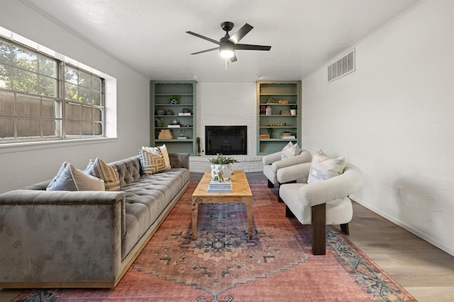 living room with wood-type flooring, a brick fireplace, ceiling fan, and ornamental molding