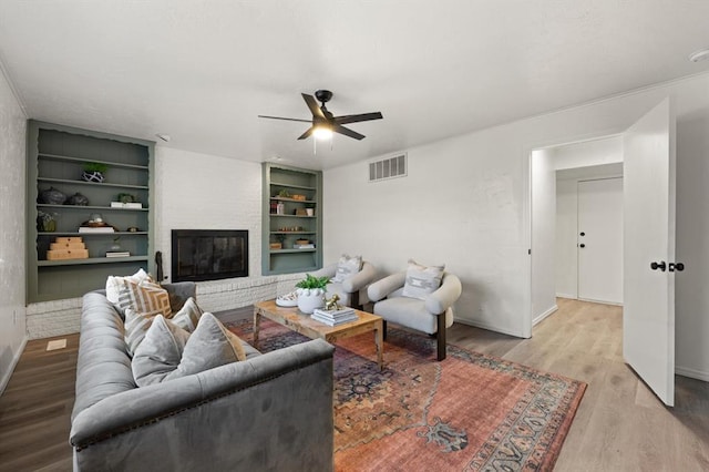 living room with ceiling fan, built in features, light hardwood / wood-style floors, and a brick fireplace