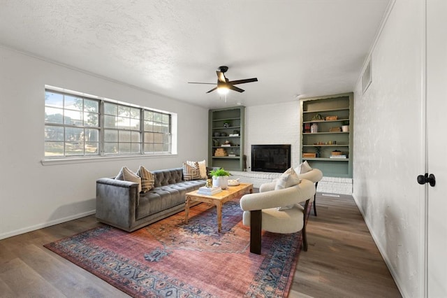 living room with a textured ceiling, a large fireplace, ceiling fan, and dark wood-type flooring