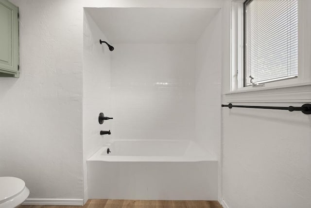 bathroom featuring wood-type flooring, tiled shower / bath combo, and toilet