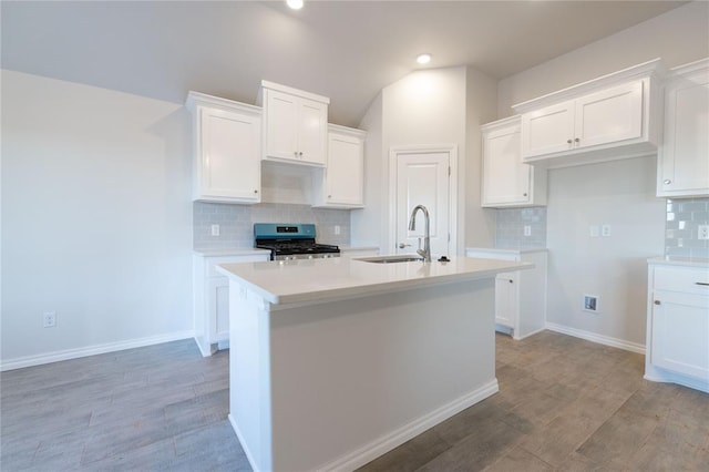 kitchen featuring stainless steel gas stove, a kitchen island with sink, light wood-style floors, white cabinetry, and a sink