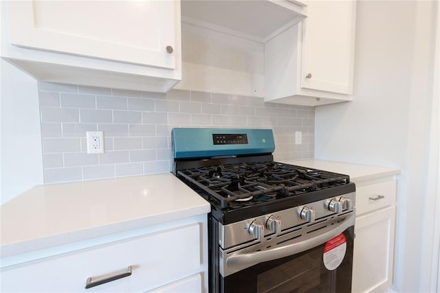 kitchen featuring stainless steel gas range, light countertops, white cabinetry, and backsplash