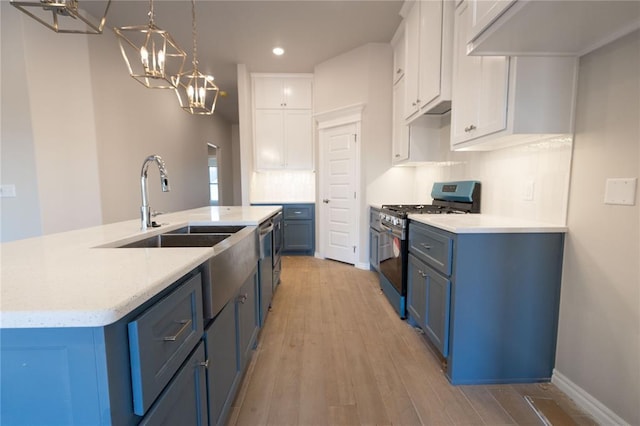 kitchen featuring stainless steel range with gas stovetop, a sink, white cabinetry, blue cabinets, and light wood-type flooring